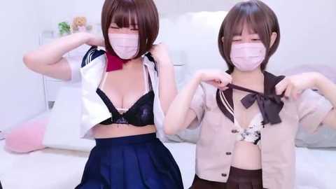 Media: A video of two young Asian women in surgical masks, unbuttoning their white blouses to reveal black bras, in a bright, minimalistic room.