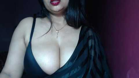 Media: Video of a woman with large, exposed breasts in a black, low-cut dress. She has long black hair and wears a gold necklace. Background is dark and indistinct.