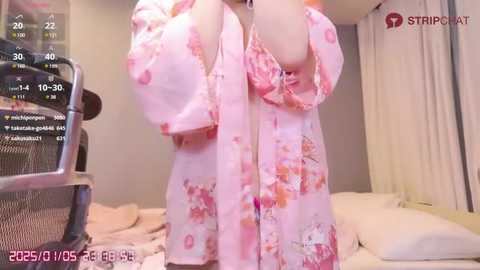 Media: A video of a person in a pink floral robe with a matching bra, standing in a modern bedroom with a bed, chair, and window.