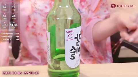 Media: A video showing a green-colored Korean rice wine bottle with a white label and Korean text, partially filled with liquid, and a person wearing a pink floral kimono in the background.