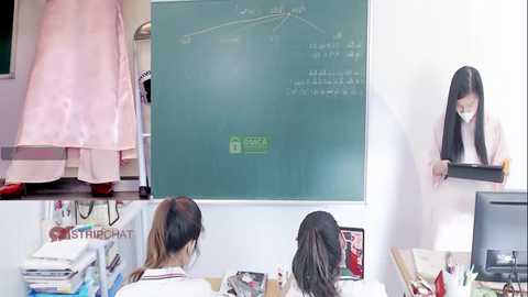 Media: Video of an Asian woman in a pink dress standing next to a classroom chalkboard, while two other women sit at desks, studying.