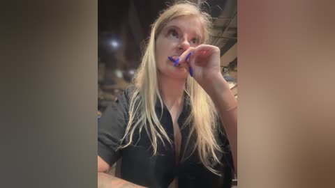 Media: Video of a blonde woman in a black shirt, brushing her teeth with a blue toothbrush, indoors at night.