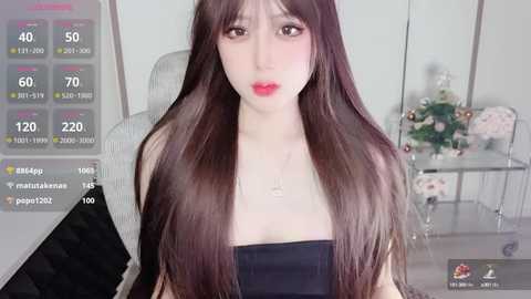 Media: Video of an East Asian woman with long, straight brown hair, fair skin, and red lipstick, wearing a black strapless top, in a modern room with white walls and a glass table.