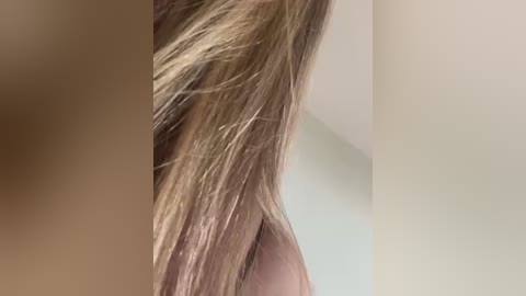 Video of a close-up of a woman's long, straight, light brown hair cascading down her back, with a blurred beige wall in the background.