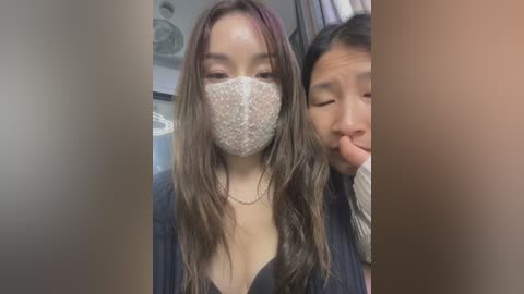 Media: A video captures two young East Asian women wearing face masks and casual attire, standing indoors. The background features a blurred bathroom setting with a sink and mirror.