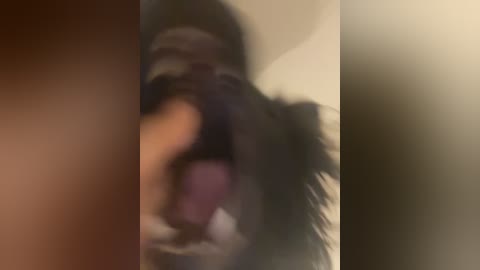 Media: A blurred video of a person with a dark complexion and dark hair, mouth open in what appears to be a distressed or shouting expression. The background is indistinct and out of focus.