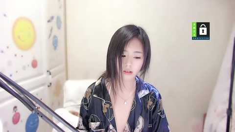 Media: A video of an East Asian woman with long black hair, wearing a partially unbuttoned, patterned robe, sitting in a bathroom with a shower curtain featuring playful designs.