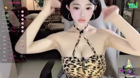 Media: Video of a young East Asian woman with fair skin and short black hair, wearing a leopard-print halter top, adjusting her hair in a dimly-lit room.