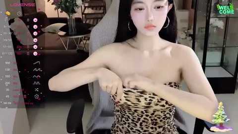 Media: A video of an Asian woman with long black hair, wearing a leopard print strapless dress, adjusting her bra in a modern living room with a couch and potted plants.