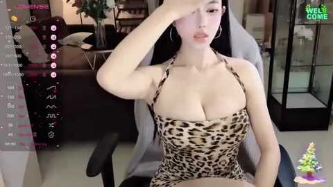 Media: Video of an East Asian woman with fair skin, wearing a revealing leopard-print halter top, sitting on a gaming chair in a modern room.