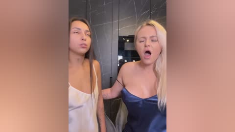 Media: Video of two young women in a modern bathroom, one in a white tank top, the other in a blue satin dress, both looking surprised.