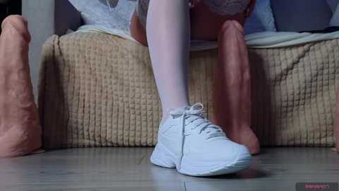 Media: A video featuring a close-up of a woman's legs in white stockings and white sneakers standing on a wooden floor. Large, realistic, pinkish-brown prosthetic legs are in the background.