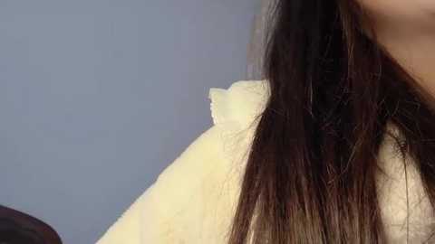 Media: A close-up video of a woman's head with long, straight dark brown hair, partially covered by a yellow towel, against a plain light blue wall background.