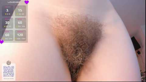 Video of a woman's pubic region, showing natural, dark pubic hair, light skin tone, and a close-up view. Background features a virtual dating app interface with heart icons and temperature gauge.