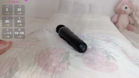 Media: A video of a black dildo on a floral-patterned bedspread in a pastel-colored room with a plush bunny toy in the background.