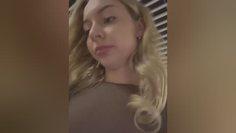 Media: Video of a young, fair-skinned woman with long, wavy blonde hair, wearing a dark top, captured from a low angle with a slightly blurry background.