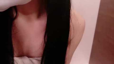 Media: A close-up video of a woman's bare upper chest, showing light skin and a hint of black hair, with a white towel partially covering her breasts.