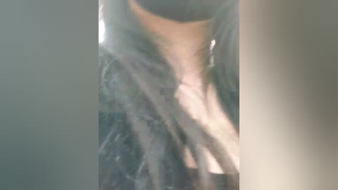 Media: A blurry video of a person wearing a black choker and a textured, dark grey garment, possibly a coat or dress, with light filtering through, creating a soft, dreamy effect.