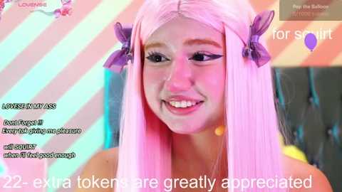 Media: A digital video featuring a smiling young woman with long, straight pink hair adorned with purple bows, wearing a sheer top. The background is vibrant with pastel colors and text overlays.