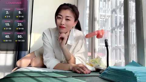 Media: Video of a fair-skinned East Asian woman in a white lab coat, resting on a green surgical table, with medical equipment and blue towels in the background.