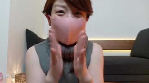 Media: A video of an Asian woman with short, dark hair, wearing a grey tank top, covering her face with both hands. She is in a modern living room with a grey couch and white walls.