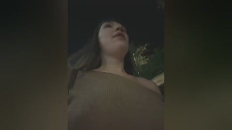 Media: Video of a young woman with long, dark hair, lying on her back, looking up at the night sky, wearing a beige top, with a blurred, dark background.