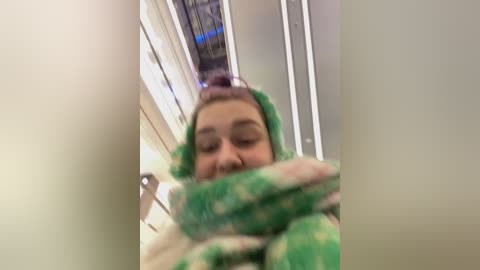 Media: Video of a young girl with light skin, wearing a green and white striped scarf, standing in a brightly lit, modern escalator with white walls and blue lighting.