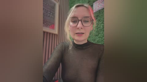 Media: Video of a fair-skinned, blonde woman with glasses wearing a sheer black top, looking through a narrow opening, surrounded by greenery and red light.