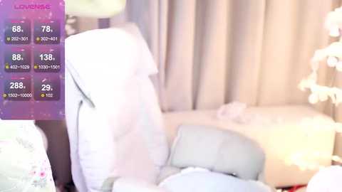 Media: Video of a cozy, well-lit bedroom featuring a white bed with fluffy pillows and a cream-colored blanket. The background includes soft, pastel curtains and a decorative lamp. The left side displays a digital thermometer with readings.