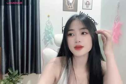 Media: Video of an Asian woman with long black hair, fair skin, and red lipstick, adjusting her hair in a modern room with white curtains, framed art, and a white chair.