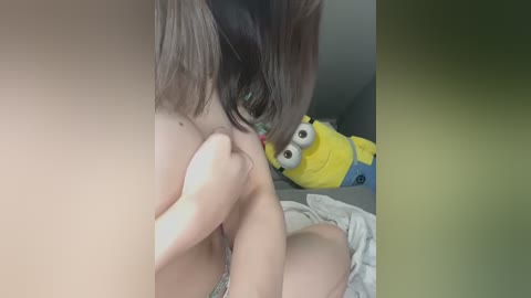 Media: A close-up video of a person with medium-length, dark brown hair, partially visible, with their breasts being sucked by another person. The background features a plush SpongeBob SquarePants toy.