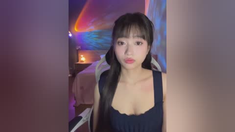 Media: A video of an East Asian woman with long black hair, wearing a black sleeveless dress, standing in a dimly lit room with a colorful abstract painting in the background.