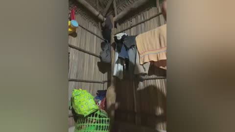 Media: Video of a rustic wooden hut with a thatched roof. A person is hanging clothes on a line, while a green laundry basket and a brightly colored bag are on the floor. The setting appears traditional and simple.