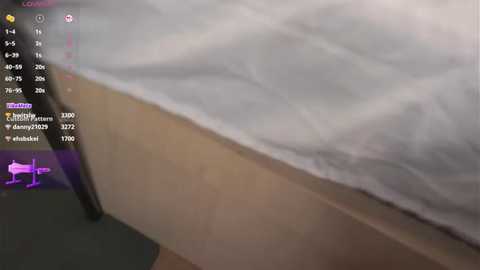 Media: Video of a bed with white sheets, displaying a live stream overlay with user information, and a small purple cow icon in the bottom left corner.