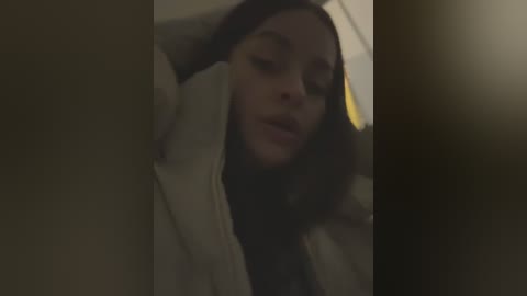 Media: A dimly lit video shows a young woman with long brown hair, wearing a beige jacket, leaning against a dark background, possibly in a car.