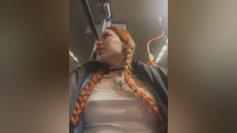 Media: A video of a young woman with long, braided orange hair, wearing a black jacket and a white tank top, seated in a subway car.