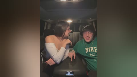 Media: Video of a woman in a white off-shoulder top, leaning on a man in a green T-shirt with \"NIKE\" and \"SNEAKERS\" in white, inside a car.