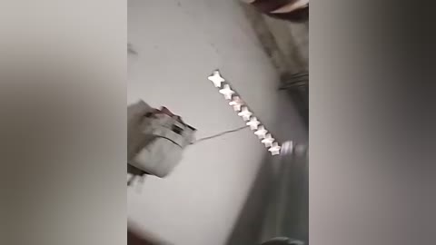 Media: Video of a mouse climbing a white wall, using a string of dangling star-shaped lights for support. The background is a cluttered, dimly lit room with visible ceiling beams. The scene evokes a sense of urgency and resourcefulness.