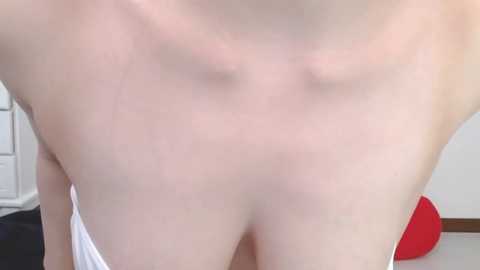 Media: A close-up video of a fair-skinned, nude individual, focusing on their chest and upper abdomen. The background includes a white door and a red object.