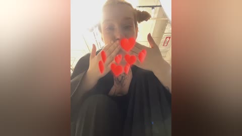 Media: A video of a young woman with fair skin and light brown hair in pigtails, sitting on a plane, covering her mouth with her hands while wearing a black jacket. Red heart emojis overlay her hands.