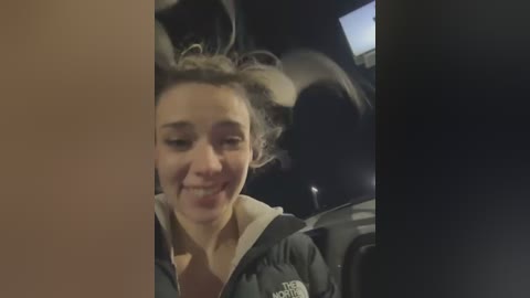 Media: A video shows a young woman with light brown hair, smiling, wearing a dark jacket, inside a car at night. The background is dark, with indistinct shapes.