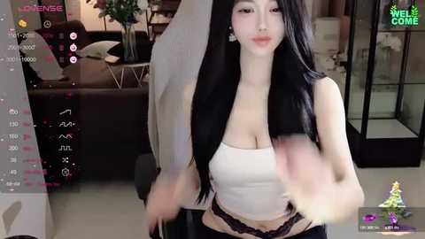 Media: A video of an East Asian woman with long black hair, wearing a white crop top and black lace panties, in a modern living room with glass doors.