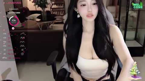 Media: A video of an East Asian woman with long black hair, wearing a white crop top, sitting in a modern living room with a Christmas tree.