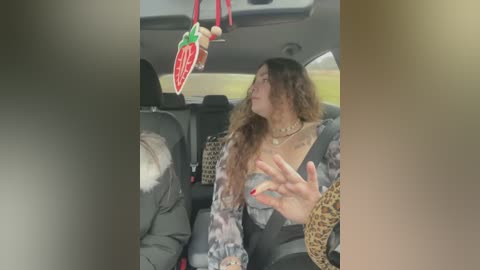 Media: Video of a woman with curly hair and a leopard print scarf, wearing a grey dress, in a car, looking out the window.