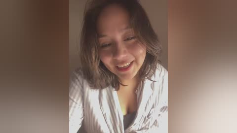 Media: A video of a smiling Asian woman with shoulder-length brown hair, wearing a striped shirt, against a blurry, neutral-toned background.