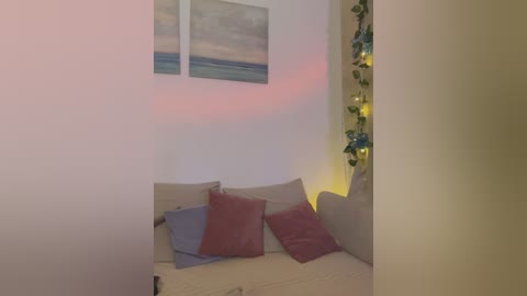 Media: A video of a cozy living room corner featuring a beige sofa with three cushions in pink, blue, and gray, a beach painting on the wall, and greenery on the side.