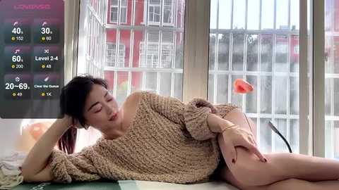 Media: Video of a serene Asian woman with dark hair, wearing a beige knit sweater, lying on a bed, watching a weather app on a tablet.