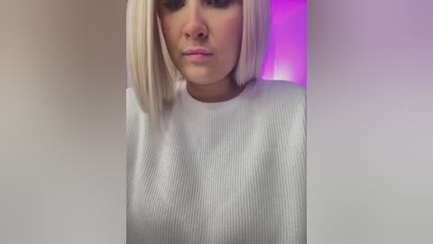 Media: Video of a fair-skinned woman with platinum blonde bob haircut, wearing a white ribbed sweater, with a purple and pink gradient background.