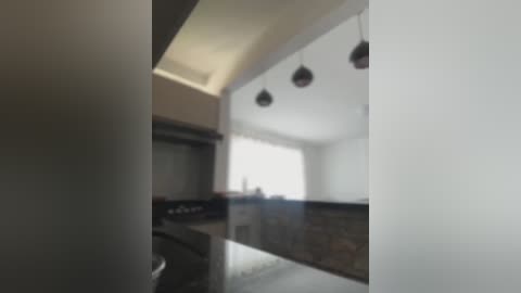 Media: A blurry, out-of-focus video of a modern, minimalist kitchen with white walls, dark countertops, and hanging pendant lights. The image is slightly overexposed, giving it a hazy appearance.