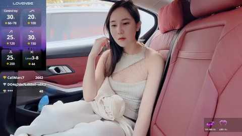 Media: Video of an Asian woman in a white, sheer dress, sitting in a red leather car seat, with a digital overlay showing her stats and heart icons.